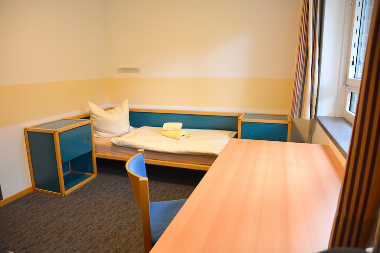 Schlafraum mit Bett, Nachtisch, Schreibtisch und einem Stuhl. 