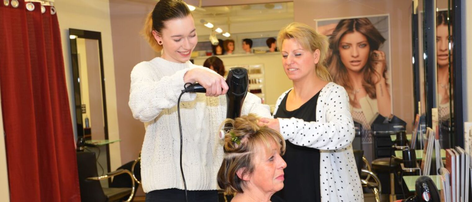 Friseur-Azubi wird beim Föhnen der Haare angeleitet