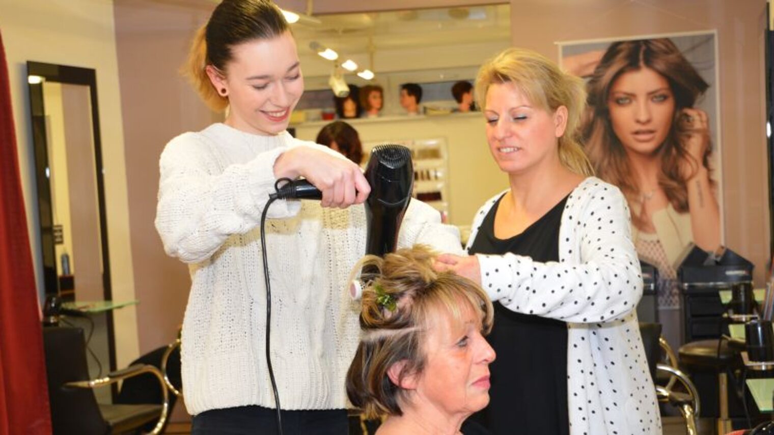 Friseur-Azubi wird beim Föhnen der Haare angeleitet