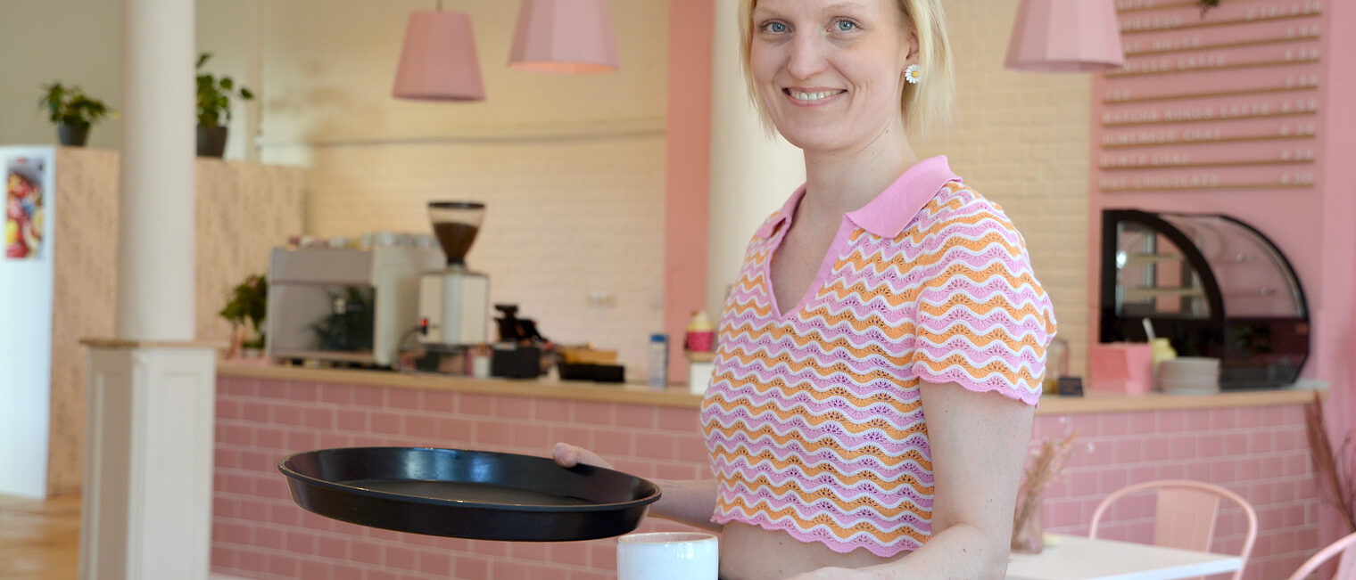 Konditorin steht in ihrem Frühstückscafé und hält eine Tasse Kaffee in der Hand.