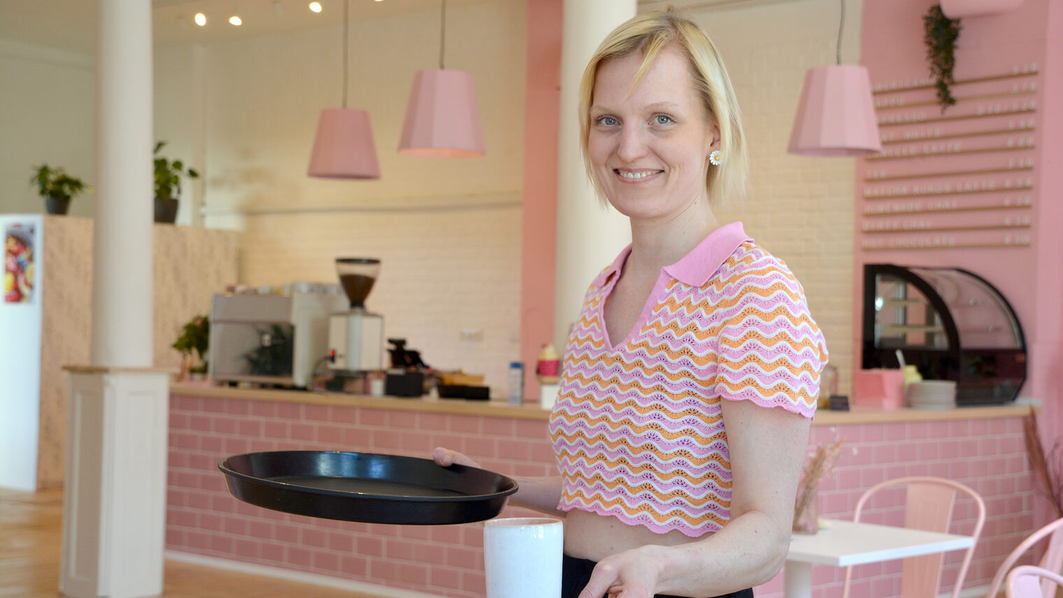 Konditorin steht in ihrem Frühstückscafé und hält eine Tasse Kaffee in der Hand.