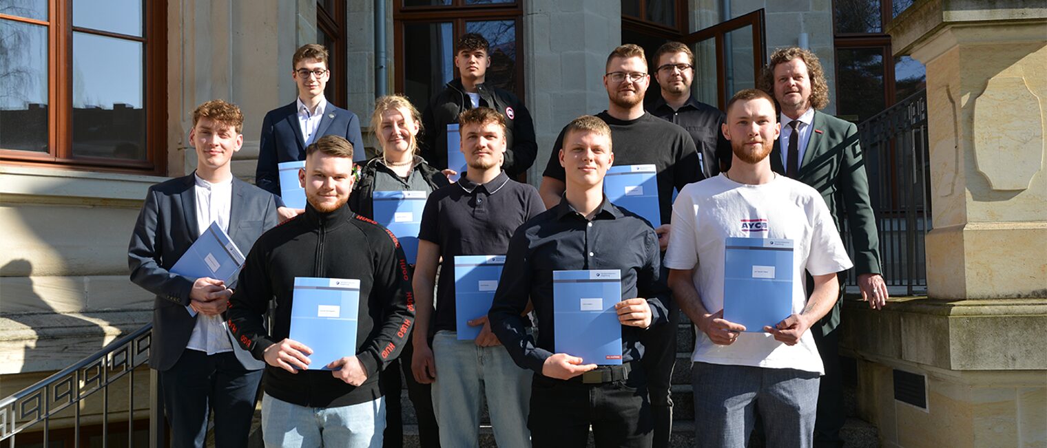 Eine Gruppe an Handwerkerinnen und Handwerker stehen vor der Handwerkskammer Magdeburg und halten ihre Weiterbildungsstipendien in den Händen.
