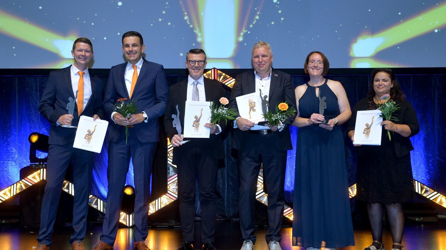 Drei Betriebs-Finalisten des Mittelstandspreises stehen auf der Bühne und halten ihren Pokal in der Nacht. 